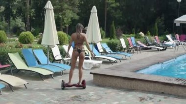 Modern genç kadın güneşli bir günde mavi yüzme havuzu yakınında Hoverboard ile yürüyüş
