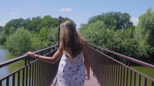Mujer sonriente caminar a lo largo de la pasarela en el pequeño puente en el parque — Vídeos de Stock