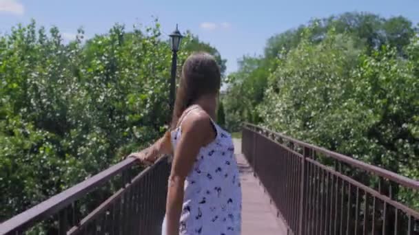 Mujer sonriente caminar a lo largo de la pasarela en el pequeño puente en el parque — Vídeos de Stock