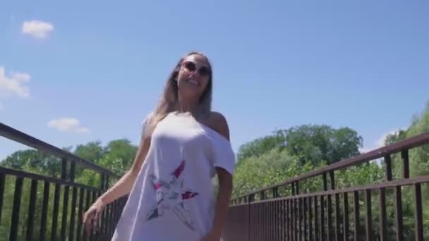 Femme souriante marcher le long de la passerelle sur un petit pont dans le parc — Video