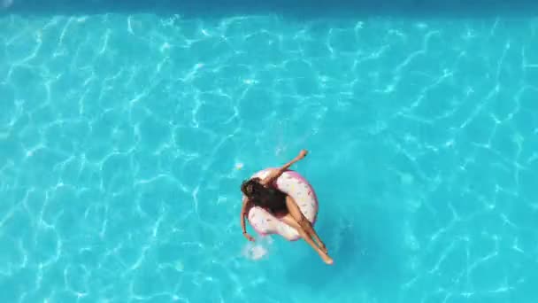 Κορίτσι στην πισίνα κολυμπά σε ένα φουσκωτό ντόνατ με ροζ χρώμα — Αρχείο Βίντεο