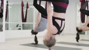 Beyaz kadınlar stüdyoda hamakta yer çekimi karşıtı yoga egzersizleri yapıyorlar. Havadan uçuş fitness antrenörü. Yaslanan Açı Pozu