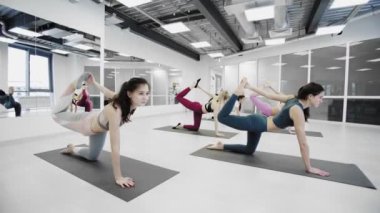 Sportif çekici kızlar, hafif sağlık stüdyosunda renkli yoga minderlerinin üzerinde otururken baş aşağı eğilerek esneme egzersizleri yapıyorlar..