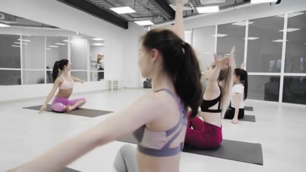 Dolly drag av Grupp av sportiga kvinnor utövar yoga lektion med instruktör, träning framför fönster och gör motion på golvet yoga studio. — Stockvideo