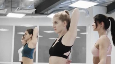 Bayan yoga öğrencisi, arkadaş canlısı neşeli kişisel eğitim eğitmeninden inek yüzüyle kol bükmeyi öğreniyor. Kadınlar konuşuyor, gülümsüyor ve pratik yapıyor..