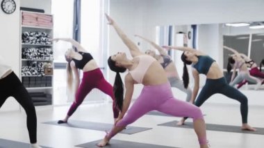 Yoga öğrencileri Virabhadrasana 'nın ışık stüdyosunda Savaşçı pozu üzerinde çalışıyorlar..
