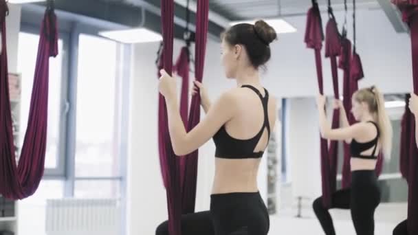 Jonge mooie yogi vrouwen doen luchtyoga praktijk in rode hangmat in fitness club — Stockvideo