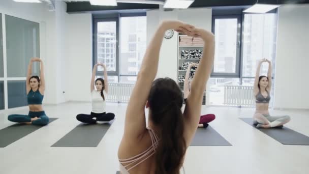 Молодая инструктор по йоге демонстрирует равновесие поз и разговаривает со студентами, в то время как другие женщины молча повторяют позы. Групповая практика . — стоковое видео