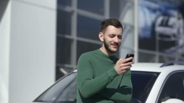 Portrait of handsome man uses his smartphone and stands near his car — Stock Video