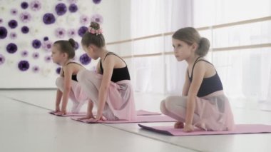 Genç balerinler yerde esneme egzersizleri yapıyor.