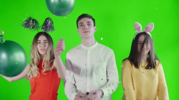 Twee mooie meisjes met grappige hoeden en jonge man dansen op groen scherm — Stockvideo