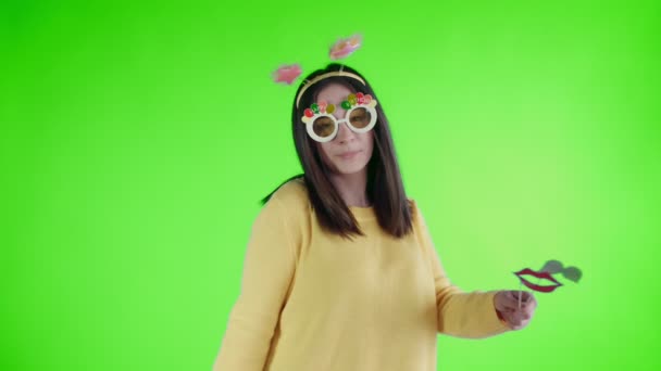 Hermosa joven con sombrero divertido y gafas es bailar solo en una pantalla verde  . — Vídeos de Stock