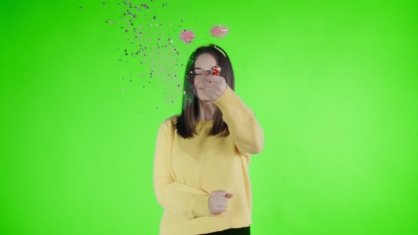 Junge Frau explodiert Konfetti-Cracker auf einer grünen Leinwand . — Stockvideo