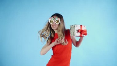 Komik gözlükleri olan genç bir kadın mavi arka planda dans ediyor.