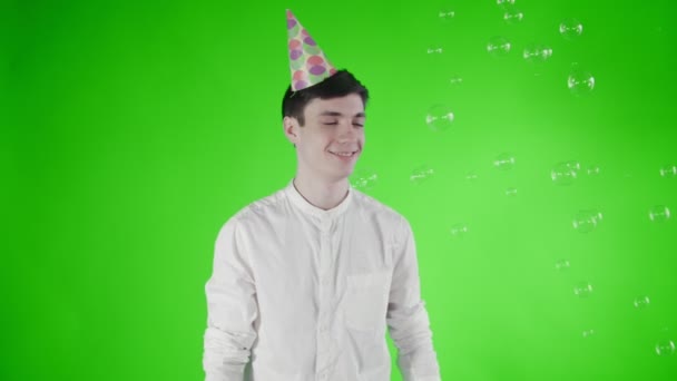 パーティー帽子をかぶった若い男は驚いています飛行泡で緑の画面 . — ストック動画