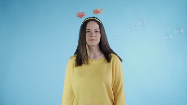 Schöne junge Frau weicht Seifenblasen auf blauem Hintergrund aus. — Stockvideo
