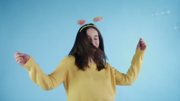 Schöne junge Frau mit lustigem Hut tanzt mit Seifenblasen auf blauem Hintergrund. — Stockvideo