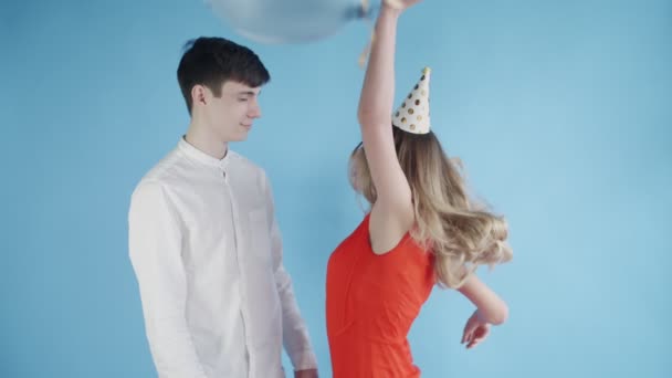 Young woman and man are dancing under colorful confetti on a blue background. — Stock Video