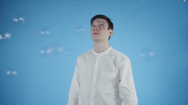 Young man in party hat are standing under soap bubble on a blue background. Slow motion — Stockvideo