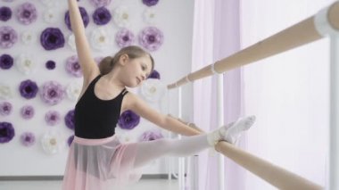 Küçük balerin, bale çubuğu tutarken geriniyor.