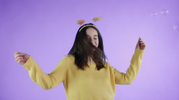 Schöne junge Frau mit lustigem Hut tanzt mit Seifenblasen auf lila Hintergrund. — Stockvideo