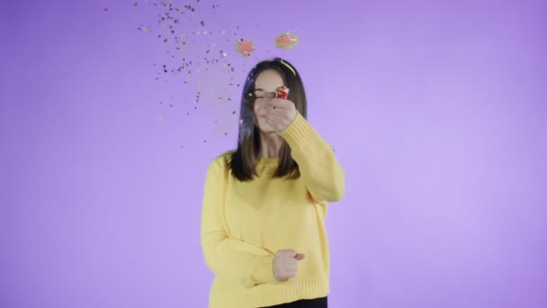 Young woman exploding confetti cracker on a purple background. — 비디오