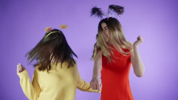 Hermosas chicas con sombreros divertidos están bailando sobre un fondo púrpura . — Vídeos de Stock