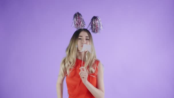 Mooi meisje in feestmuts en kartonnen snor dansen op een paarse achtergrond. — Stockvideo