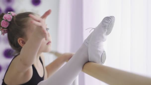 Маленькие девочки используют балетную планку, когда делают упражнения на растяжку ног в танцевальной студии — стоковое видео