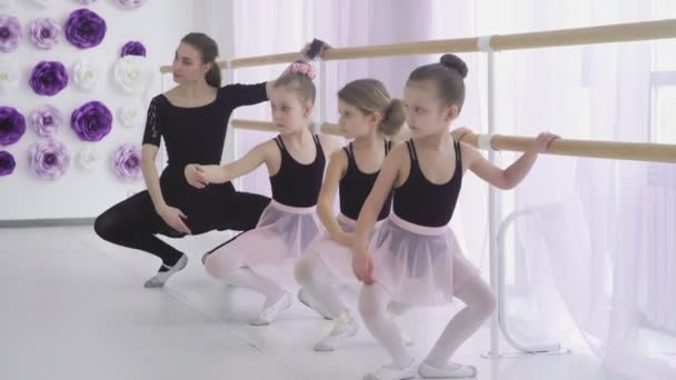 Yoğunlaşmış kızlar dans okulunda temel bale pozisyonlarını öğreniyorlar. Dikkatli bir öğretmen zor duruşlarda ustalaşmalarına yardımcı oluyor.. — Stok video