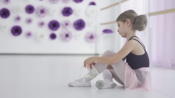 Young ballet dancer tying ballet shoes before training — Stock Video