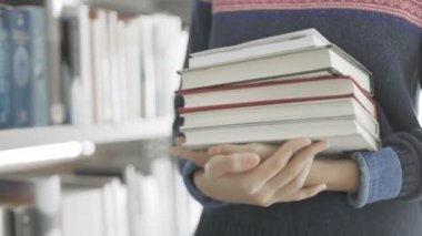 Genç Afrikalı Amerikalı kadın elinde bir sürü kitap tutuyor.