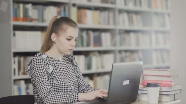 Chica seria estudiante trabajando en el ordenador portátil con libro en la biblioteca de la ciudad — Vídeos de Stock