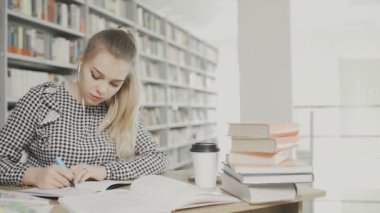 Kadın kütüphanede kağıda yazıyor.