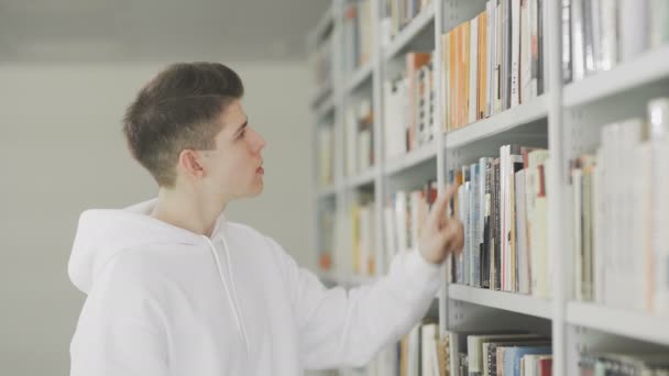 Man op zoek naar boek op boekenplanken in de bibliotheek op de universiteit — Stockvideo