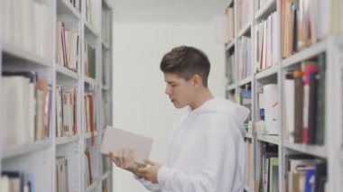 Kütüphanedeki kitaplıktan kitap alan öğrenci
