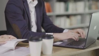 Genç Yakışıklı Adam kütüphanede dizüstü bilgisayarda oturuyor ve çalışıyor. Masada bir fincan kahve.