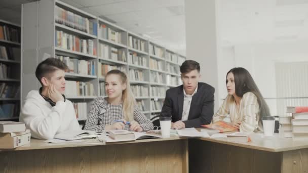 Studenci pracujący razem przygotowując się do egzaminów siedząc przy stole w bibliotece uniwersyteckiej — Wideo stockowe