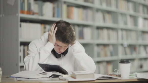 Zmęczony student przygotowuje się do egzaminu w bibliotece uniwersyteckiej — Wideo stockowe