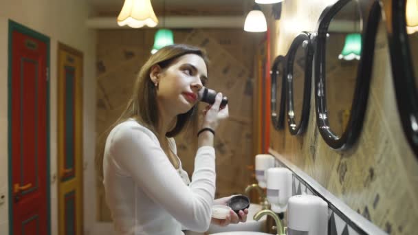 Женщина наносит косметику с большой щеткой в туалете общежития — стоковое видео