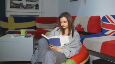 Kanepenin yanında kitap okuyan güzel bir kadın. Üzerinde bayraklar ve yastıklar var.