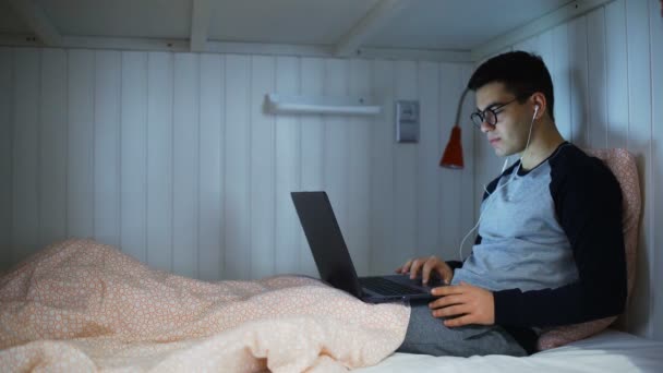 Hombre joven que trabaja en el ordenador portátil en la cama en la habitación del albergue — Vídeo de stock