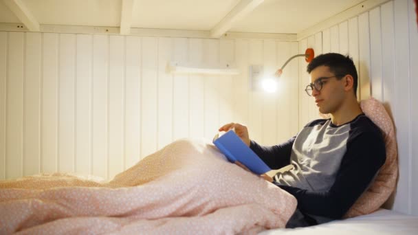Человек, читающий книгу на кровати в общежитии комнате — стоковое видео