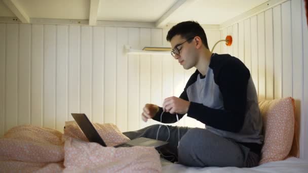 Jeune homme regardant la vidéo sur ordinateur portable au lit dans la chambre de l'auberge — Video