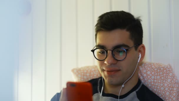 Atractivo y guapo joven con una hermosa sonrisa se desplaza a través de las redes sociales se alimentan en el teléfono inteligente, risas y sonrisas de las noticias en las aplicaciones — Vídeos de Stock