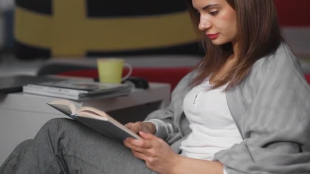 Dolly verhuizing van vrouw het lezen van een boek op de vloer in de buurt van bank met kussens met land vlaggen — Stockvideo