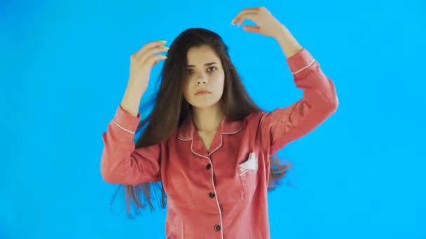 Retrato de una joven en pijama tocándose el pelo aislado sobre fondo azul — Vídeos de Stock