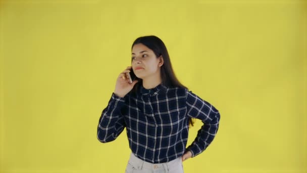 Mujer joven de pie aislada sobre fondo amarillo mientras habla por teléfono — Vídeos de Stock