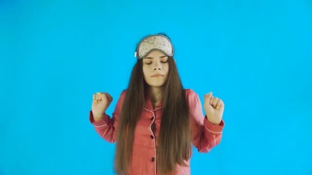 Νεαρό όμορφο κορίτσι με πιτζάμες χασμουρητό και τέντωμα σε μπλε φόντο στο στούντιο — Αρχείο Βίντεο
