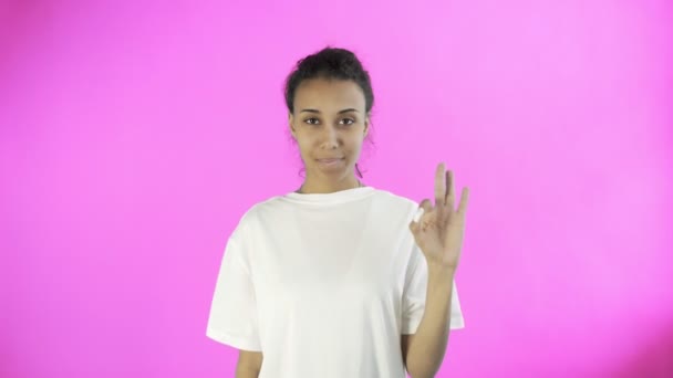 CuteAfro-American Girl está mostrando ok com dois polegares e sorrindo no fundo rosa no estúdio — Vídeo de Stock